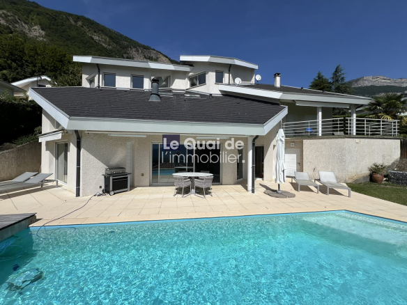 Modern two-story white house with a beige patio and bright blue swimming pool in the foreground, mountain backdrop.