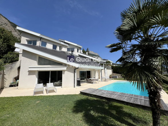 Modern two-story house with white exterior, large glass doors, and a rectangular blue pool in the sunny backyard.