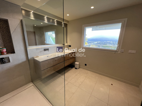 Modern bathroom with a glass shower, floating wood vanity, and a large window showing a city and hills view outside.