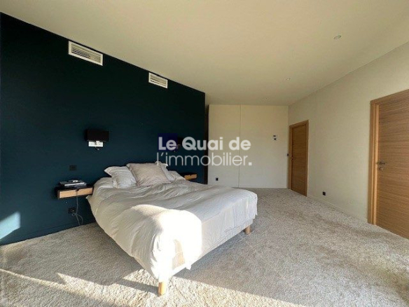 Modern bedroom with a white bed against a dark teal accent wall and side shelves, on a light carpeted floor. Two wooden doors are visible in the background.