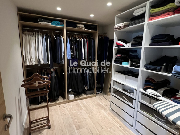Walk-in closet with open wardrobes on left and built-in shelves on right, clothes folded on shelves and hanging garments visible.