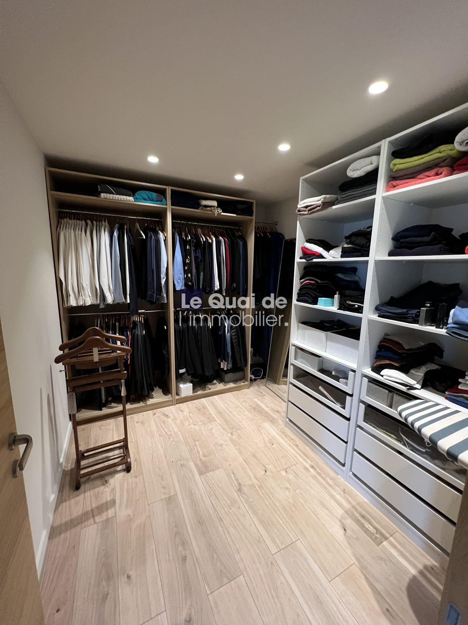 1770966327_VM8231_11_original Walk-in closet with open wardrobes on left and built-in shelves on right, clothes folded on shelves and hanging garments visible.