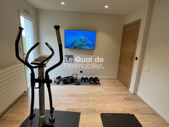 Home gym with an elliptical trainer on a black mat, free weights and kettlebells along the wall, and a wall-mounted TV.