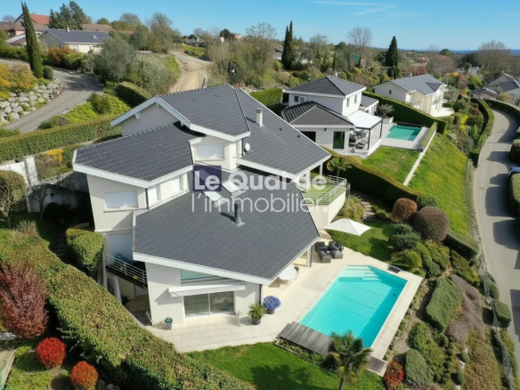 A modern white villa with a dark tiled roof and a rectangular turquoise pool in a landscaped hillside yard in bright daylight, aerial view.