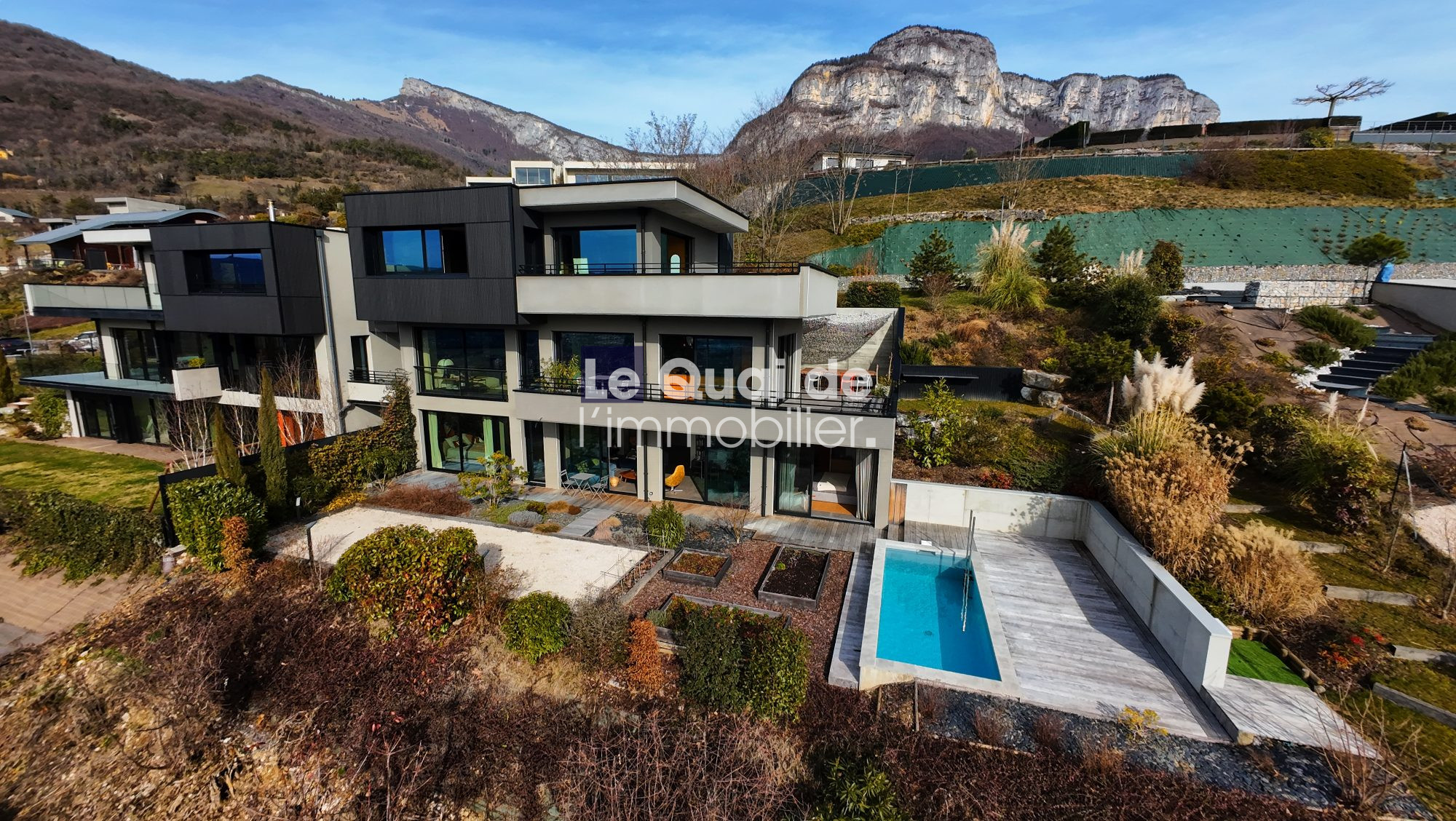 1771603298_VM8233_1_original A modern multi-story villa with a rectangular pool, glass doors, and landscaped garden, set against rocky hills in the distance.