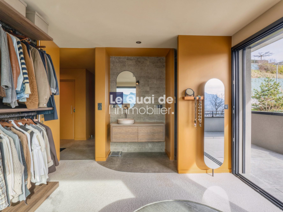 Walk-in closet with orange walls, clothes on racks to the left, a wooden vanity with a round sink in the center, and a glass door opening to an outdoor terrace on the right.