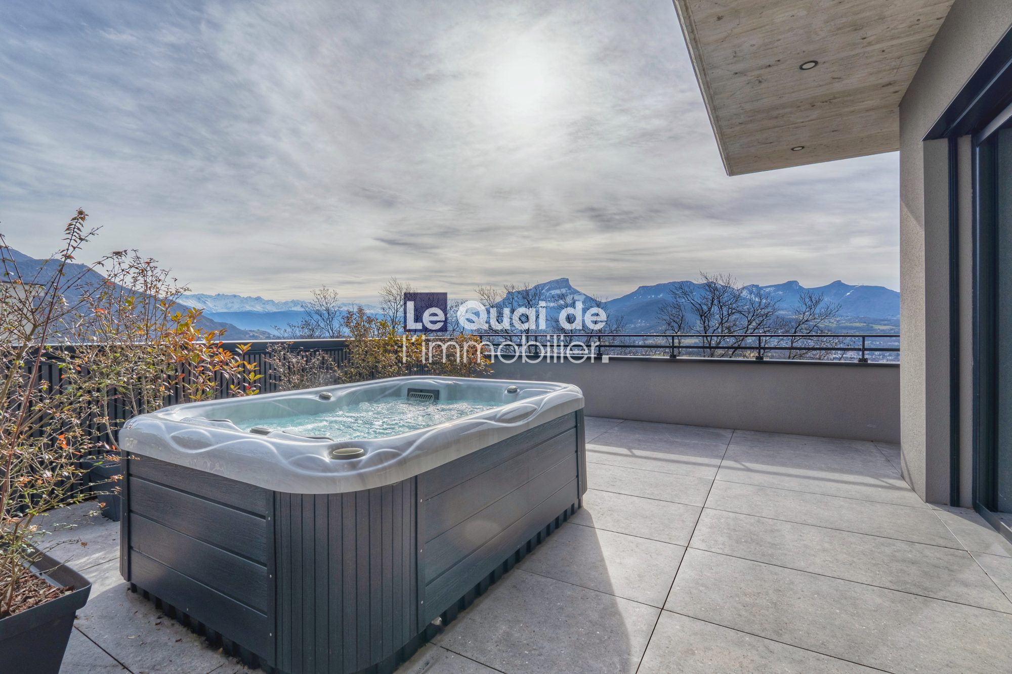 1771603305_VM8233_6_original Modern balcony with a hot tub overlooking a mountain range under a cloudy sky.