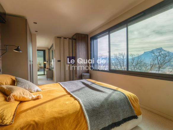 Modern bedroom with mustard bedding, throw blanket, and several pillows, large bay window showing mountains outside.