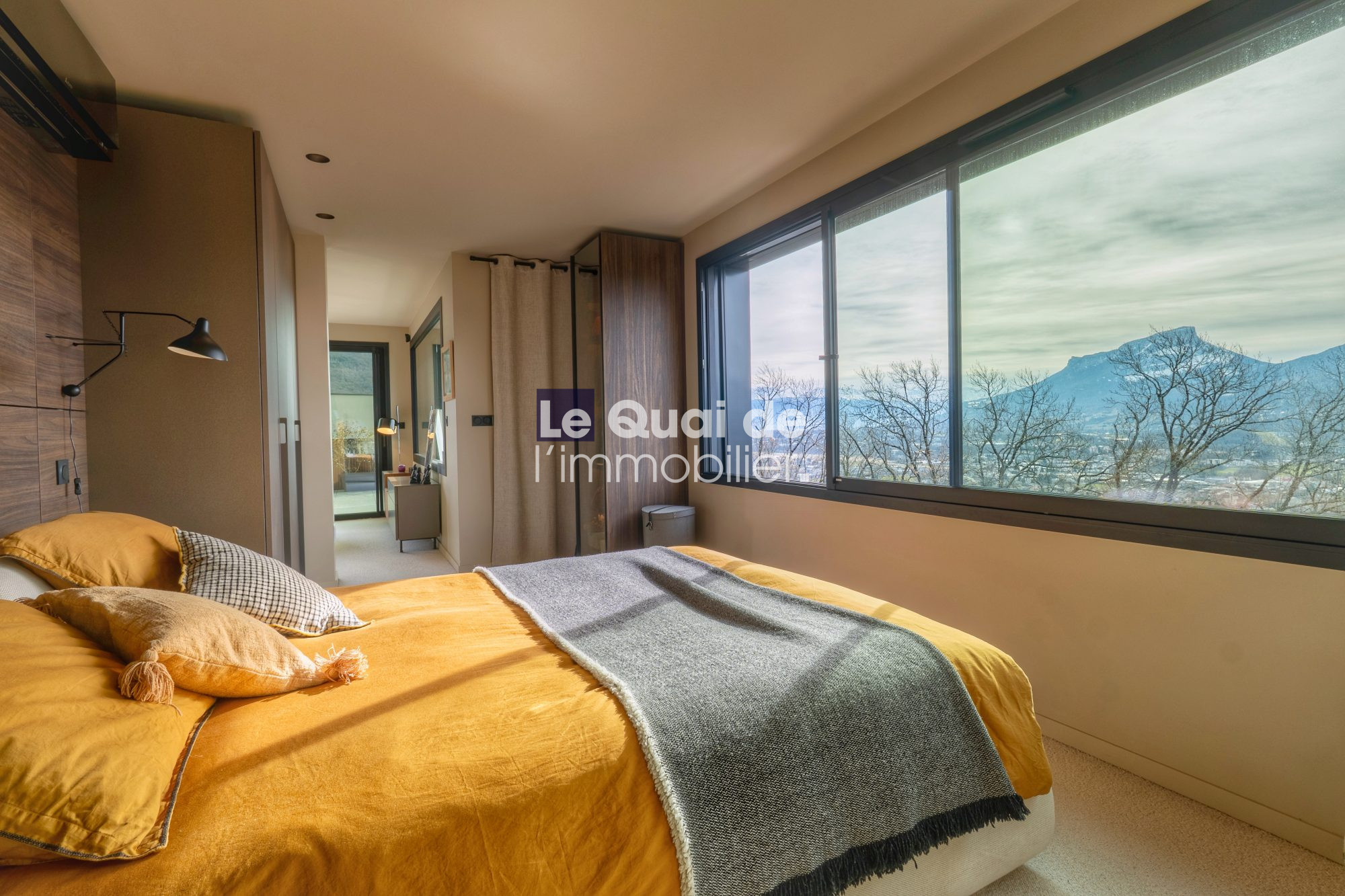 1771603310_VM8233_9_original Modern bedroom with mustard bedding, throw blanket, and several pillows, large bay window showing mountains outside.