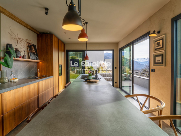 Modern kitchen with a long concrete island, warm wooden cabinets, and sliding glass doors to a mountain view outside.