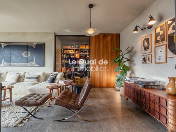 Modern living room with a beige sectional, brown leather lounge chair and ottoman, and a wooden sideboard; gallery wall and a tall plant contribute to a cozy, stylish space.
