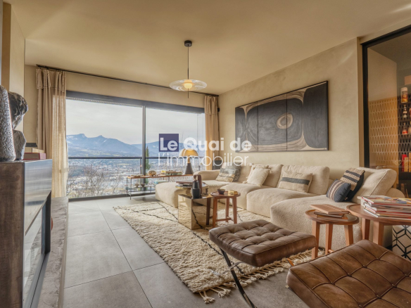 Bright living room with a beige sectional, cream rug, and a large window showing mountains and a lake outside.