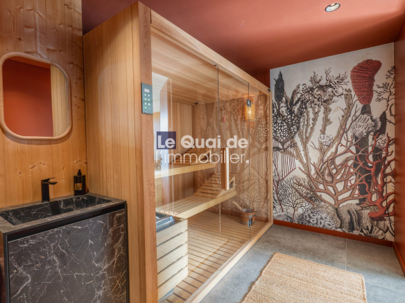 Wood-paneled sauna with a glass-front door, wooden benches, and a black marble sink area to the left; coral reef mural on the right wall.
