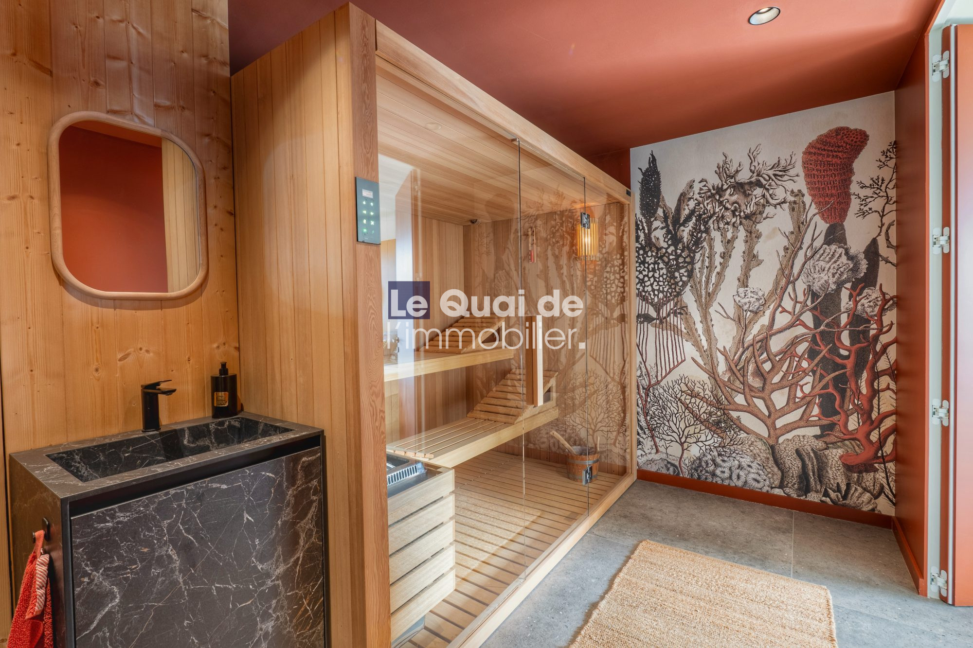 1771603326_VM8233_20_original Wood-paneled sauna with a glass-front door, wooden benches, and a black marble sink area to the left; coral reef mural on the right wall.