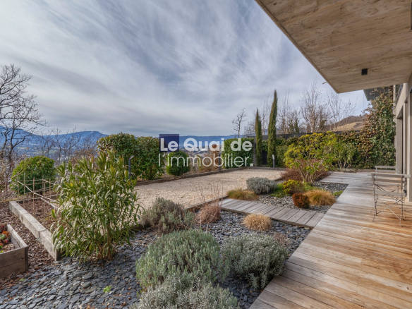 Wooden deck patio with a landscaped garden and distant mountains along the hedge line.