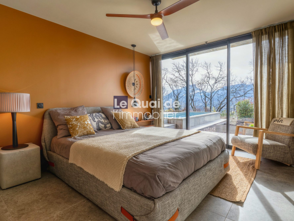 Bedroom with orange accent wall, gray upholstered bed, beige throw, and large glass doors opening to a pool and mountain view.