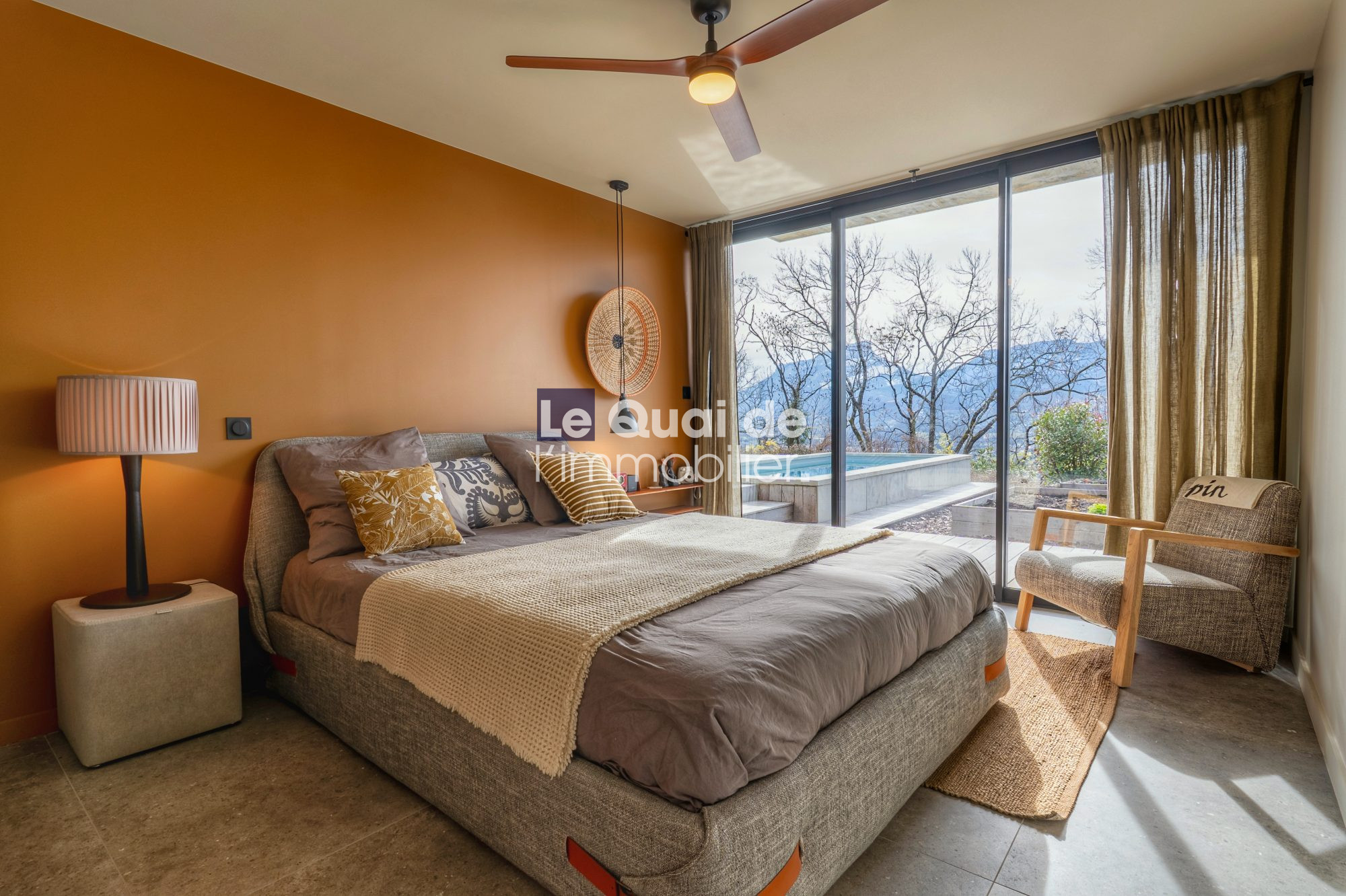 1771603334_VM8233_26_original Bedroom with orange accent wall, gray upholstered bed, beige throw, and large glass doors opening to a pool and mountain view.