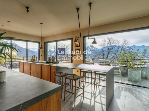 Modern kitchen with a long island, wooden cabinets, and large windows showing a mountain landscape outside (open-plan dining area).