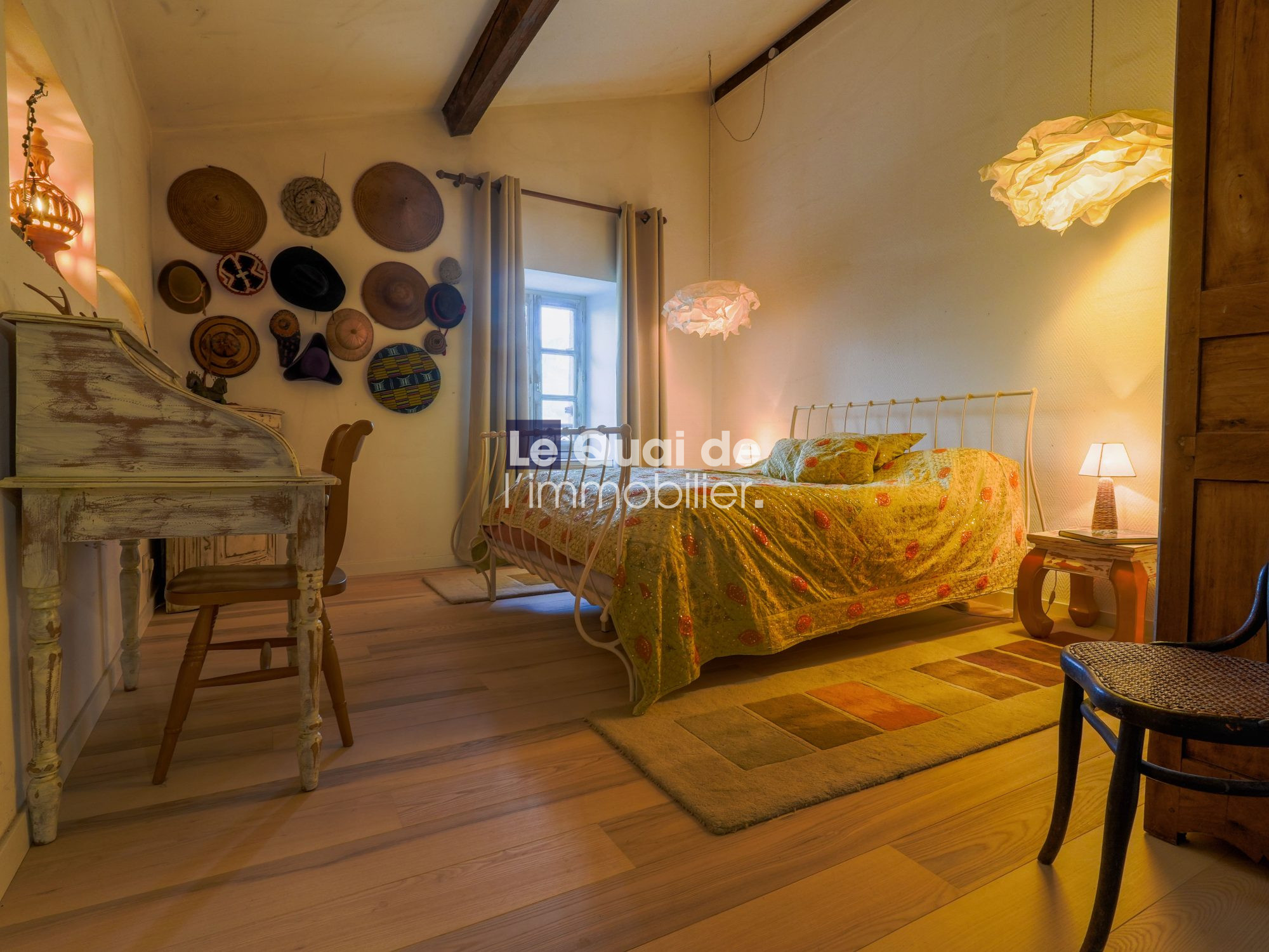 Cozy vintage bedroom with a metal bed, colorful quilt, and a wall display of hats.