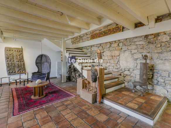 Interior of a rustic gallery with stone wall, wooden ceiling beams, and eclectic sculptures around a red patterned rug and round coffee table at center.