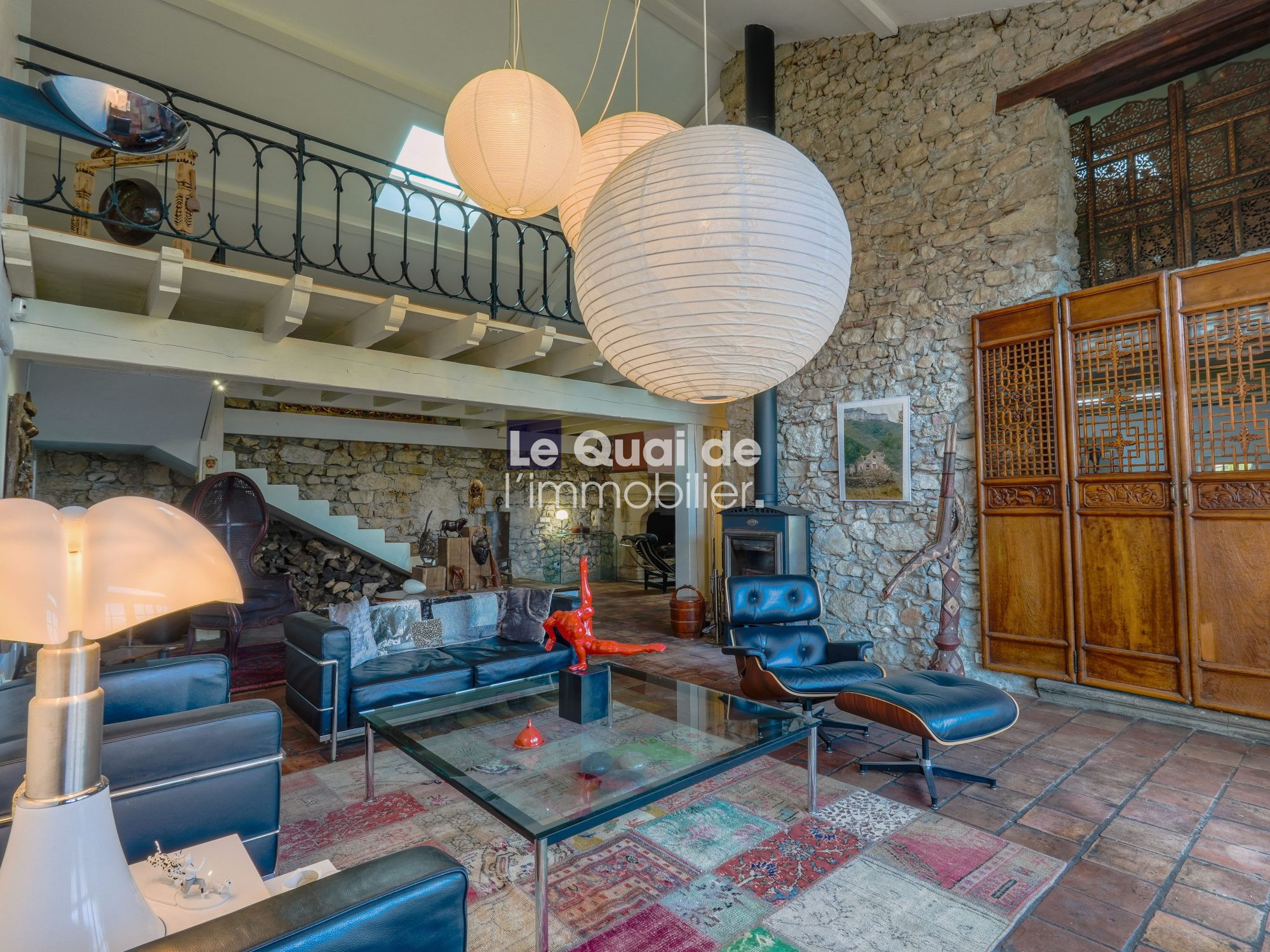 Loft-style living room with stone walls, a white paper lantern centerpiece, and blue leather seating around a glass coffee table.