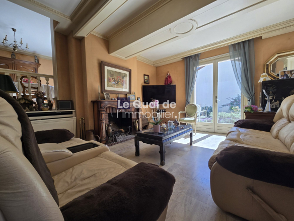 Cozy living room with beige leather sofas, a dark wood coffee table, and a brick fireplace; glass doors open to a sunny garden.