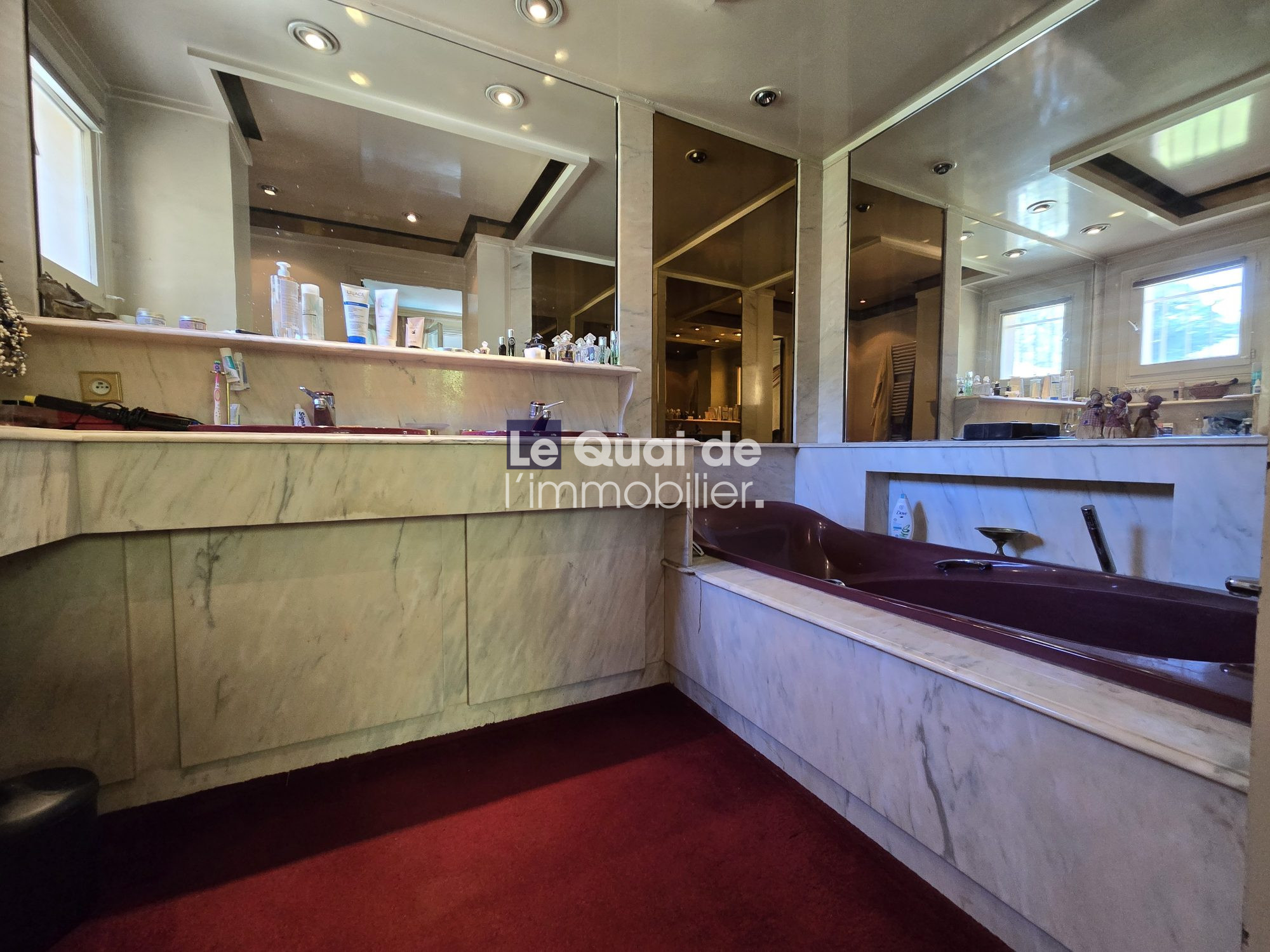 Luxurious marble bathroom with built-in soaking tub and mirrored walls; toiletries arranged on the counter and windows in the background.