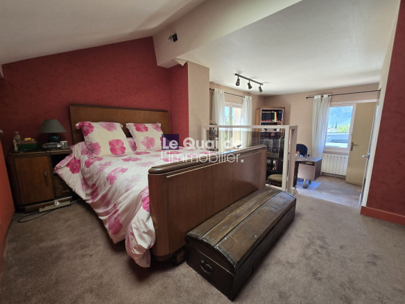Bedroom with a red accent wall, a wooden headboard bed in floral pink bedding, and a dark wooden chest at the foot of the bed.