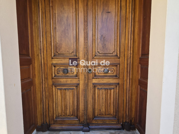 Double tall wooden doors with paneled carvings at a building entrance; a tiled threshold and a dirt mat in front.