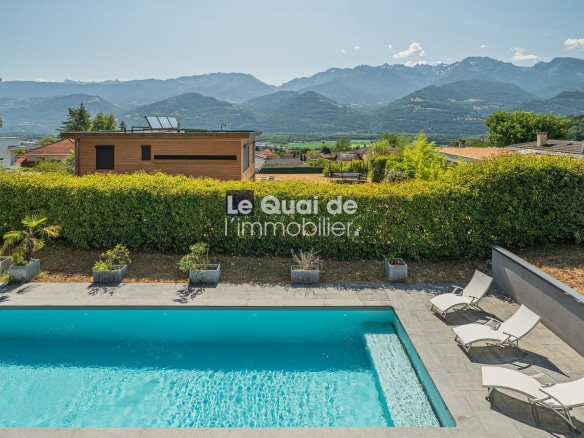 Vue de la piscine et des terrasses d'une villa d'architecte à Bernin avec les montagnes en arrière-plan.