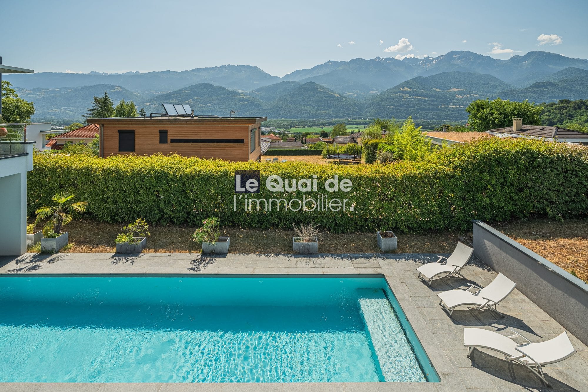 Vue de la piscine et des terrasses d'une villa d'architecte à Bernin avec les montagnes en arrière-plan.