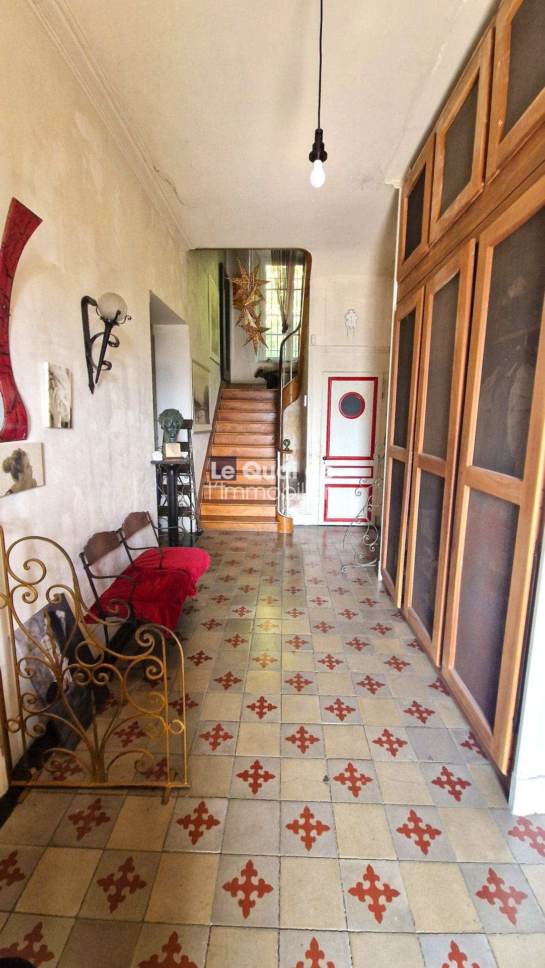Intérieur d'une maison de maître avec carrelage ancien et escalier en bois.