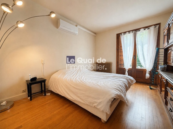 Chambre d'une maison à vendre à Drumettaz-Clarafond, avec un lit et des fenêtres donnant sur l'extérieur.