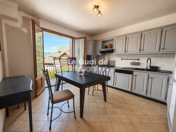 Cuisine d'une maison à vendre à Drumettaz-Clarafond, avec table et chaises, fenêtres ouvertes sur l'extérieur.