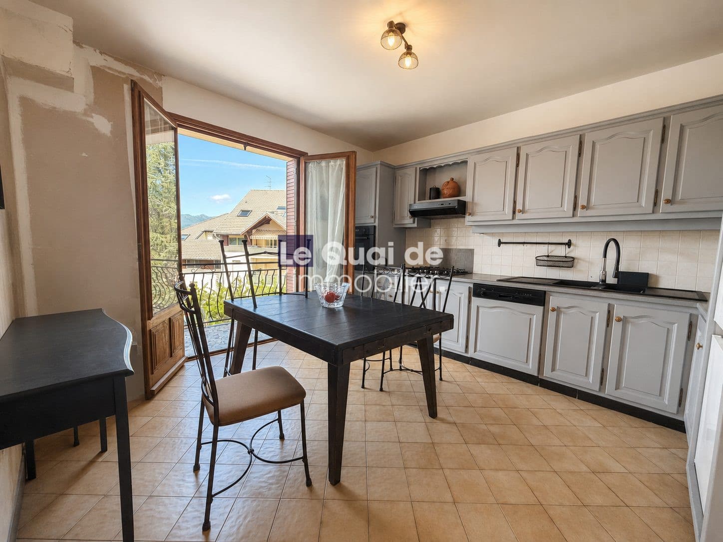 Cuisine d'une maison à vendre à Drumettaz-Clarafond, avec table et chaises, fenêtres ouvertes sur l'extérieur.