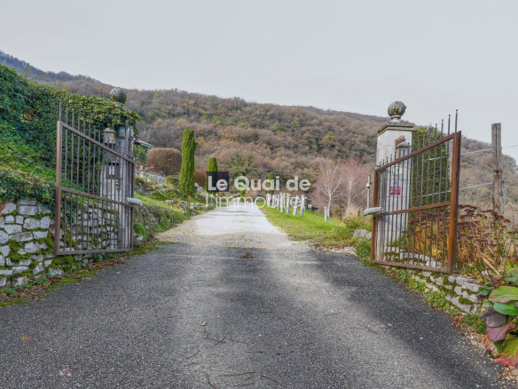 Entrée d'une propriété avec portail en fer et chemin menant à une bâtisse du XVIIe siècle.
