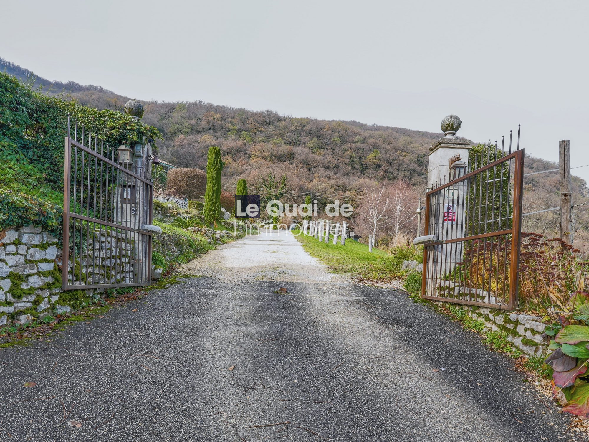 Entrée d'une propriété avec portail en fer et chemin menant à une bâtisse du XVIIe siècle.