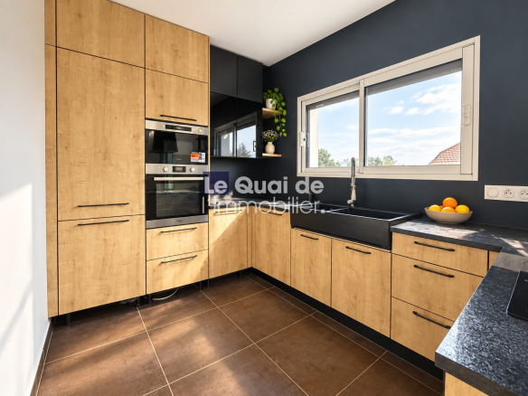 Cuisine moderne avec meubles en bois et plans de travail noirs, fenêtre laissant entrer la lumière.