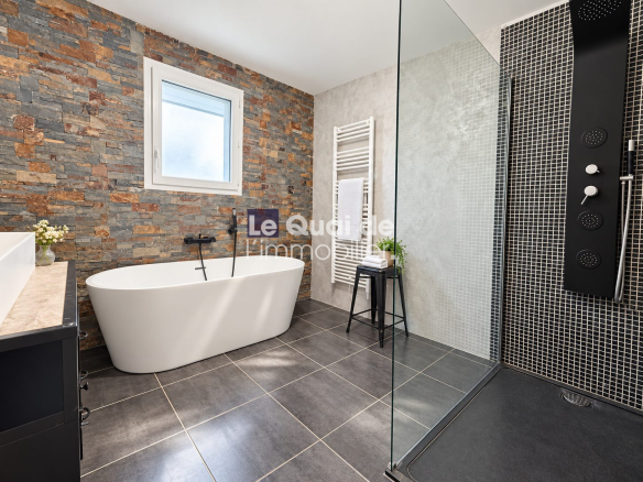 Salle de bain moderne avec baignoire sur pied et douche à l'italienne, murs en pierre et carrelage noir.
