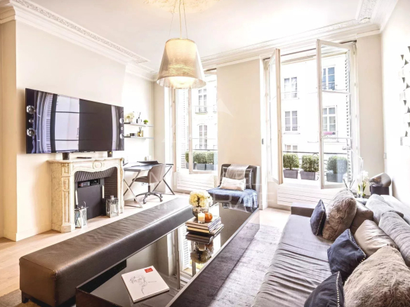 Salon lumineux d'un appartement à Paris avec cheminée et fenêtres ouvertes sur rue.