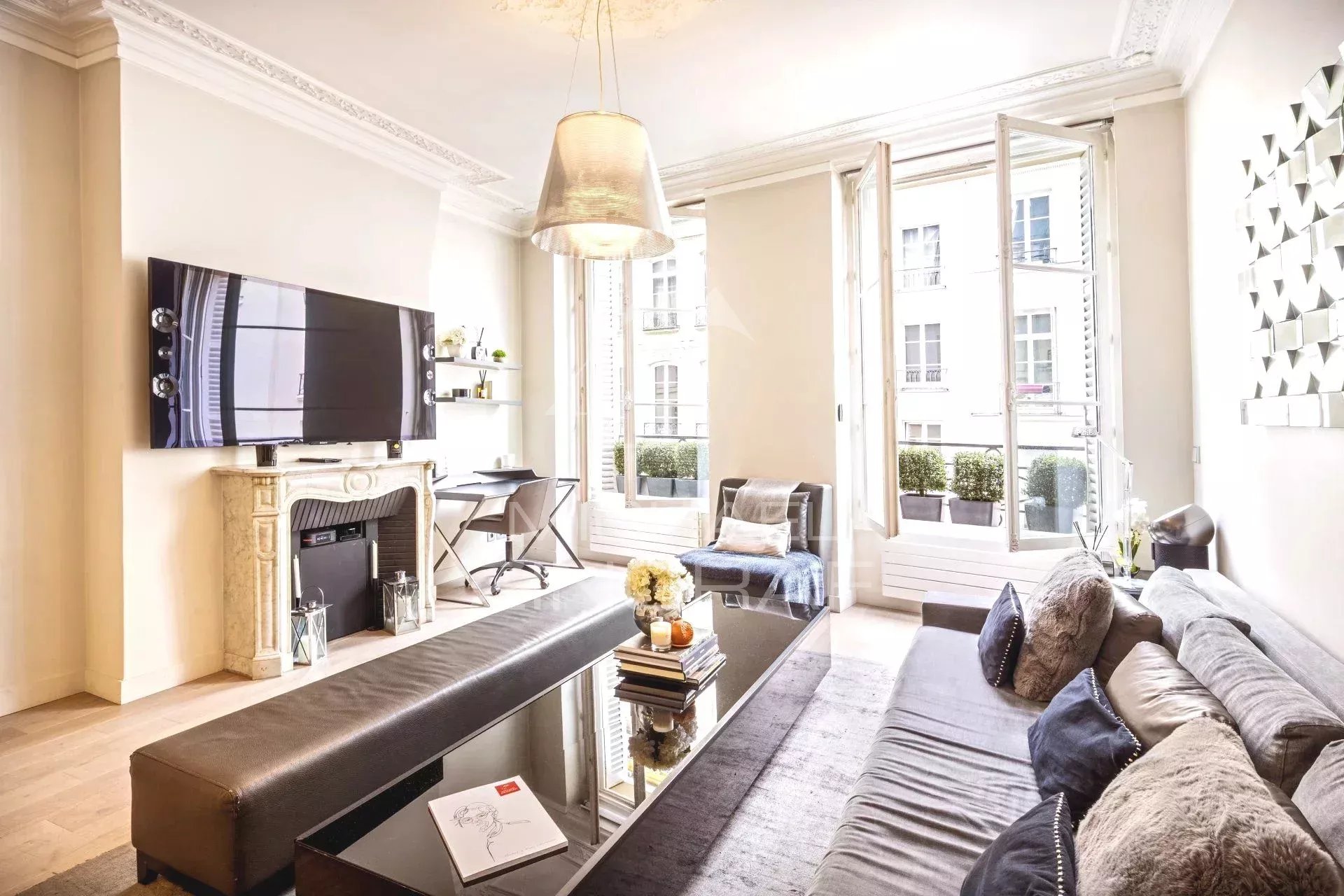 Salon lumineux d'un appartement à Paris avec cheminée et fenêtres ouvertes sur rue.