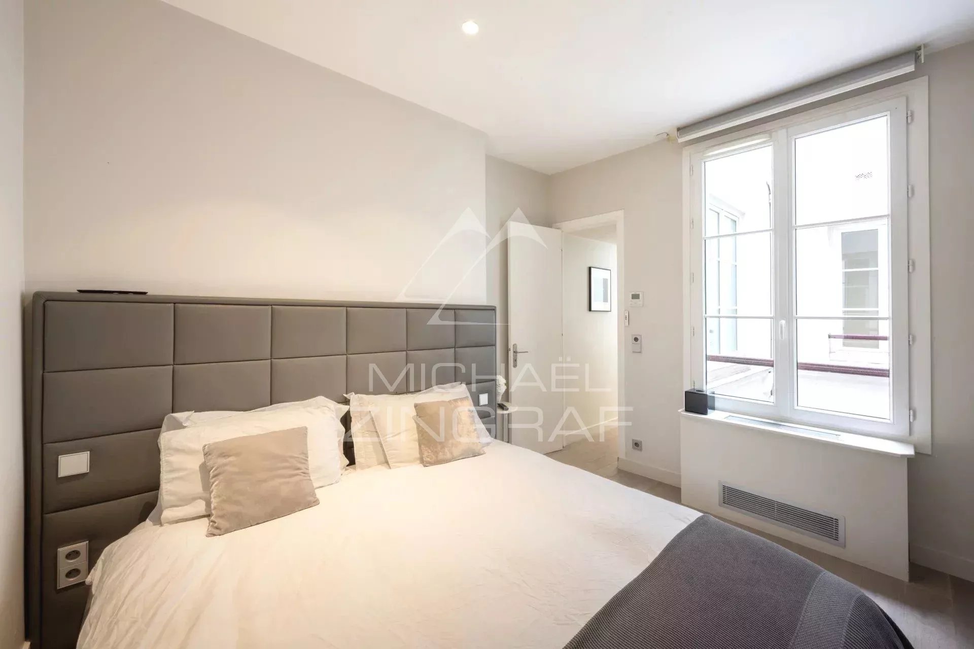 Chambre d'un appartement moderne avec lit double et fenêtre à Paris 1er.