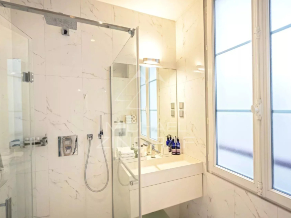 Salle de bain moderne avec douche en verre et lavabo, lumière naturelle à travers une fenêtre.