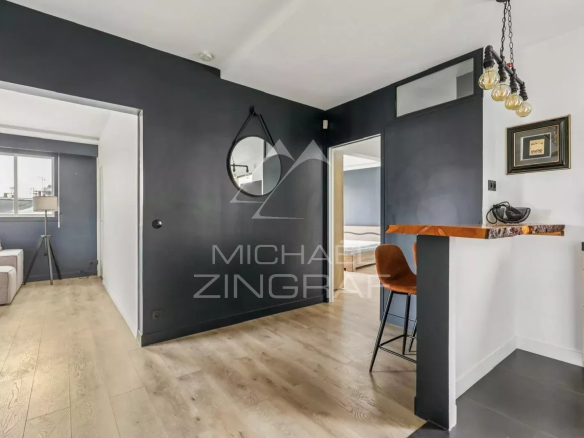 Intérieur d'un appartement moderne avec un coin salon et un bar, murs sombres et lumière naturelle.