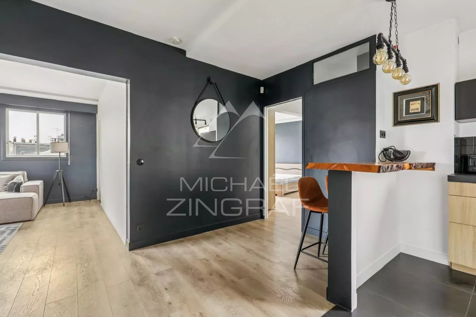 Appartement à vendre à Paris 16ème Intérieur d'un appartement moderne avec un coin salon et un bar, murs sombres et lumière naturelle.