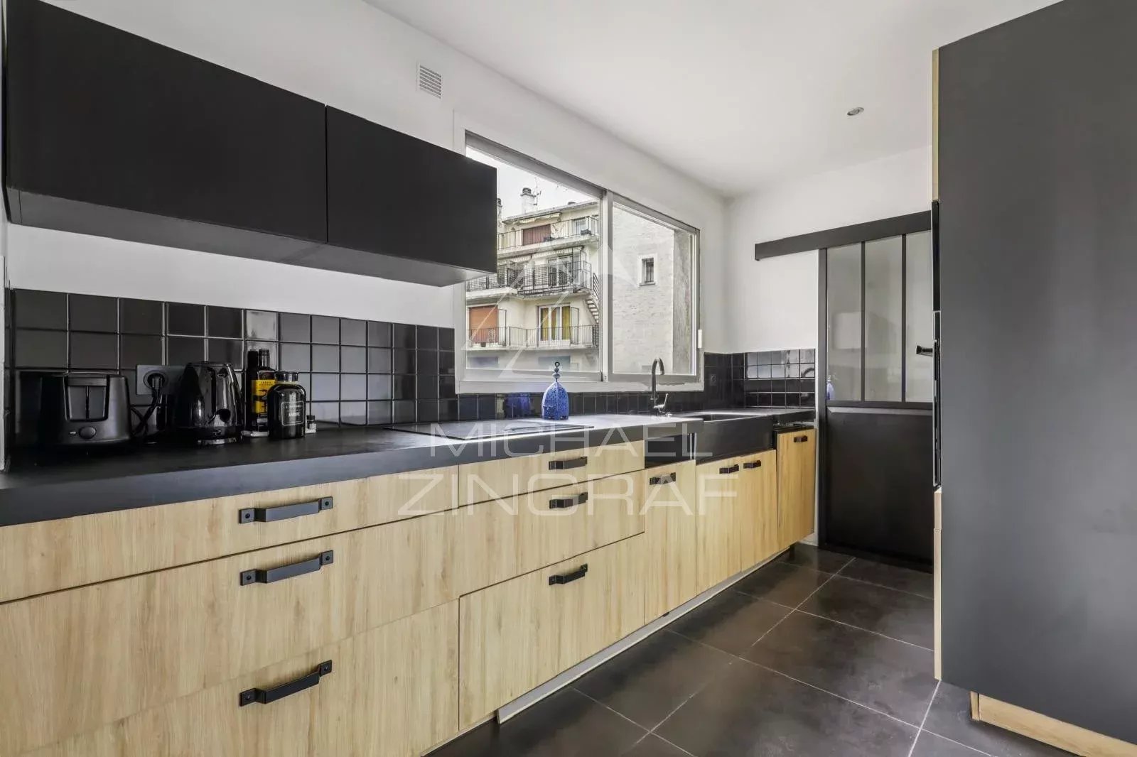Cuisine d’un appartement à vendre à Paris 16ème Cuisine moderne avec meubles en bois et noir, fenêtre donnant sur l'extérieur.