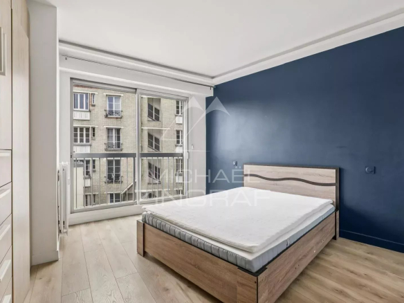 Chambre d'appartement à vendre avec balcon, Paris 16ème, murs bleu foncé et parquet clair.