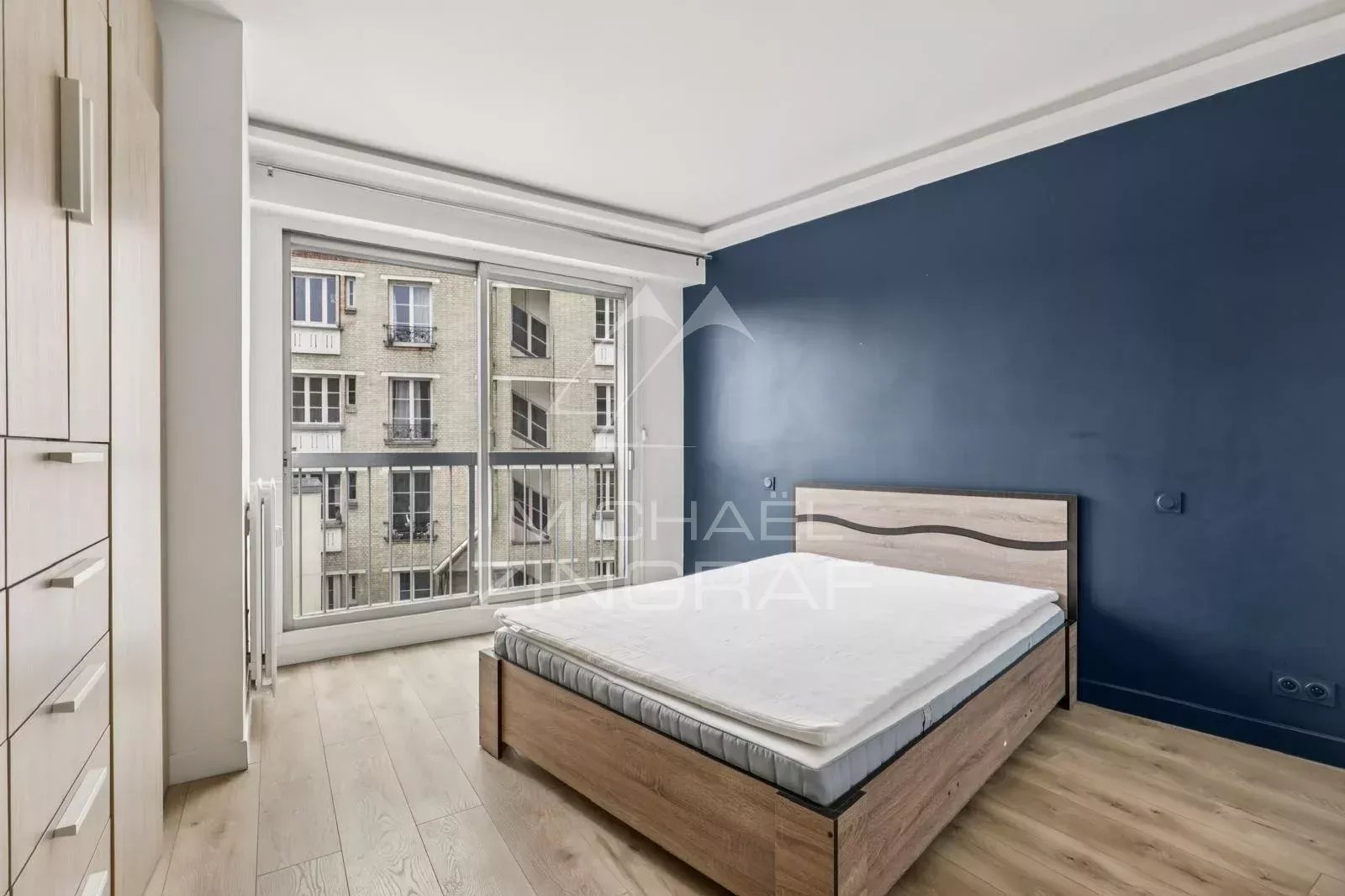 Chambre à vendre à Paris 16ème Chambre d'appartement à vendre avec balcon, Paris 16ème, murs bleu foncé et parquet clair.