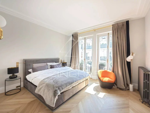 Chambre d'un appartement rénové avec lit double, fauteuil orange et fenêtres donnant sur l'extérieur.