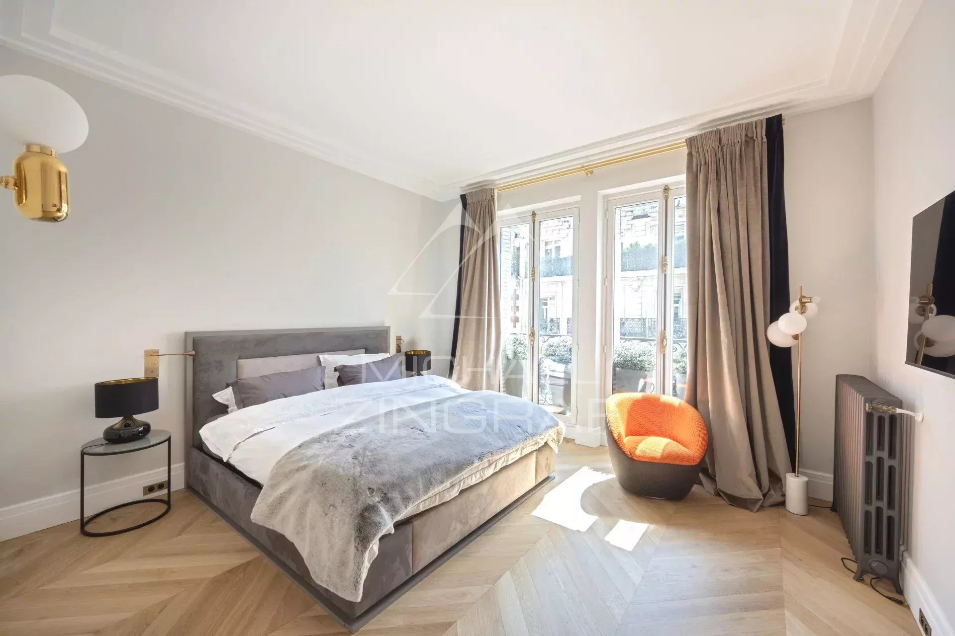 Chambre d’appartement rénové à Paris Chambre d'un appartement rénové avec lit double, fauteuil orange et fenêtres donnant sur l'extérieur.